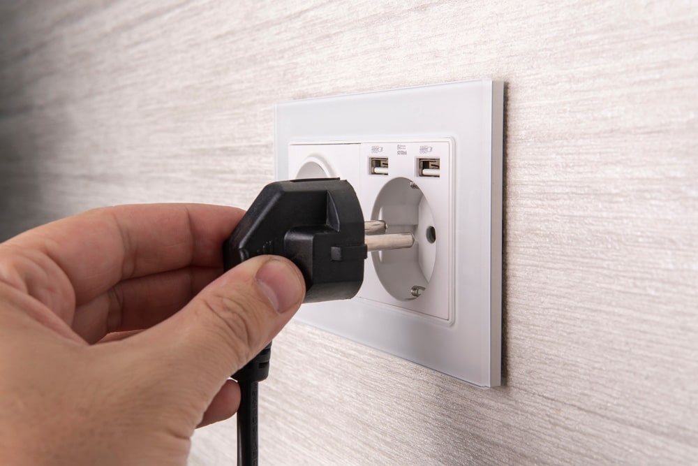 Hand plugging in an electric cord into a European wall outlet